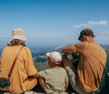 Family sitting on a rock, enjoying a panoramic view of the Tatra Mountains under clear blue skies.
