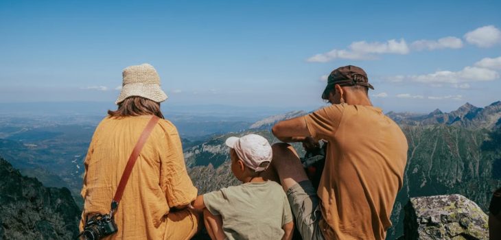 Family sitting on a rock, enjoying a panoramic view of the Tatra Mountains under clear blue skies.